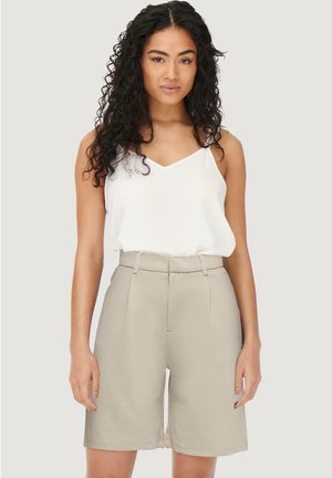 Lichtbeige op maat gemaakte shorts met een hoge taille en zijkantenzakken, gecombineerd met een witte cami met dunne bandjes. Gladde, matte textuur.