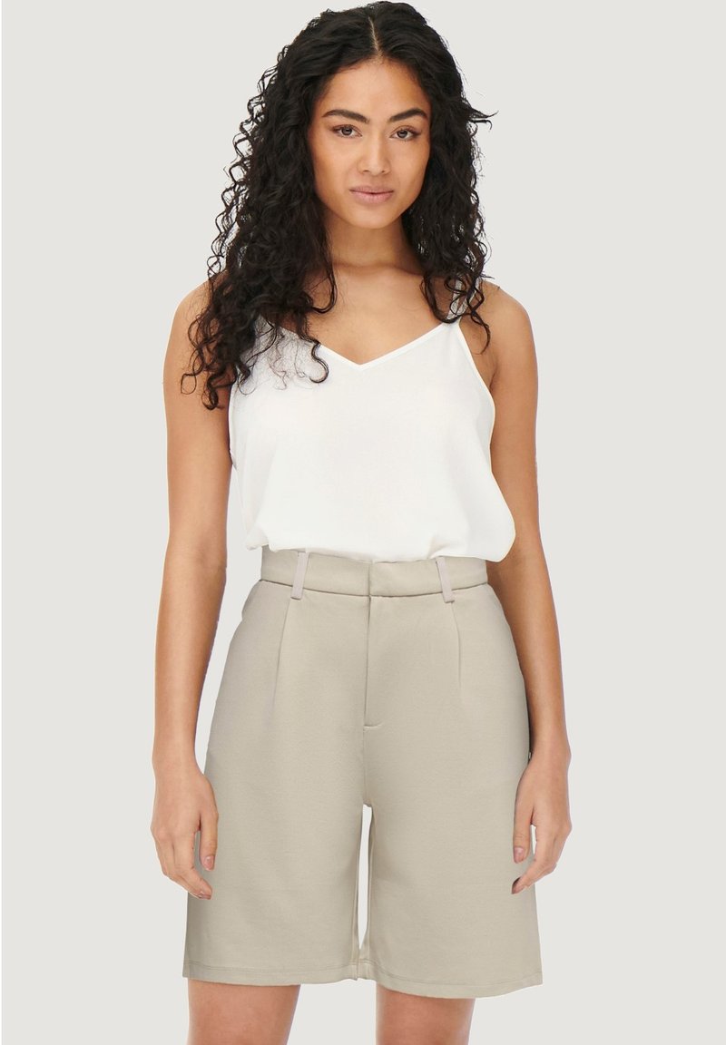 Lichtbeige op maat gemaakte shorts met een hoge taille en zijkantenzakken, gecombineerd met een witte cami met dunne bandjes. Gladde, matte textuur.
