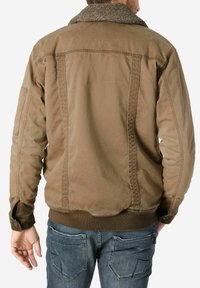 Braune Baumwolljacke mit Schafslederkragen. Verfügt über Knöpfe an den Ärmeln, seitliche Taschen und einen gerippten Saum. Sieht leicht getragen aus und hat eine strukturierte Oberfläche.