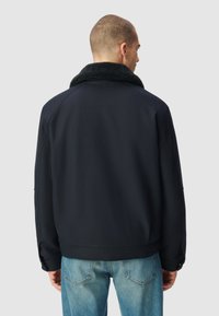 Chaqueta azul marino con un suave cuello negro, diseñada con un dobladillo recto y mangas raglán, combinada con jeans de mezclilla claros.