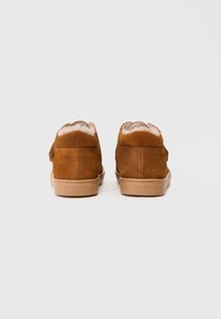 Braune Wildleder-Stiefeletten mit einem weichen Fellfutter, flachen Gummisohlen und gewellten Kanten am Knöchel, ausgestattet mit seitlichen Klettverschlüssen.