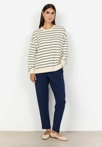 Randig, krämfärgad tröja med svarta linjer, kombinerad med marinblå tapered-byxor och mjuka beige ballerinaskor. Enkel, avslappnad passform med upprullade ärmar.