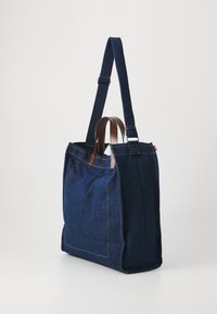 Denim draagtas met bruine leren accenten en een donkerblauwe kleur. Beschikt over een stevige rechthoekige vorm en dubbele schouderbanden.