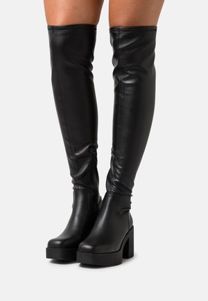 Botas negras por encima de la rodilla hechas de cuero suave, con un tacón ancho, cremallera lateral y un ajuste ceñido con un diseño elegante.
