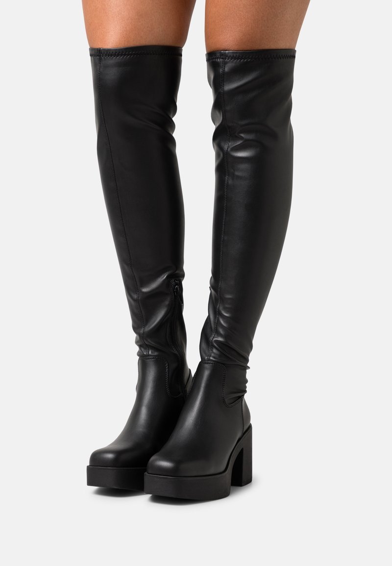 Botas negras por encima de la rodilla hechas de cuero suave, con un tacón ancho, cremallera lateral y un ajuste ceñido con un diseño elegante.