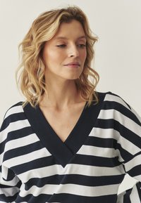 Top a righe blu navy e bianche con scollatura a V, realizzato in un tessuto morbido e maniche ampie. Presenta un colletto blu navy a tinta unita.
