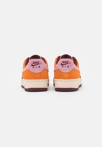 Nike Air-sneakers har en orange ovandel i mocka, rosa bakre flik och detaljer, mörkbrun yttersula och gräddfärgad mellansula för kontrast.