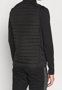 Schwarze leichte Weste mit gepolstertem gestepptem Design auf der Rückseite, featuring einen hohen Kragen und langen Ärmeln aus einem glatten Stoff.