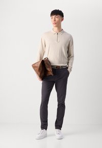 Beige rits polo shirt, donkergrijze broek, witte sneakers en een bruin leren tas. Eenvoudig ontwerp met een gladde textuur en subtiele accenten.