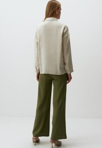Licht beige overhemd met lange mouwen en kraag, gecombineerd met olijfgroene wijde broek. Glad textuur, casual snit en minimale ontwerpparameters.
