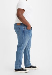 Vaqueros de mezclilla azul claros con un corte recto, diseño de cinco bolsillos y una cintura texturizada, combinados con zapatillas negras y una camiseta blanca.