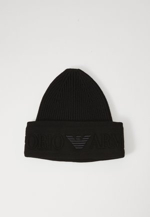 Bonnet en tricot noir avec une texture côtelée et un revers, arborant un design de logo en relief en matériau sombre à l'avant.