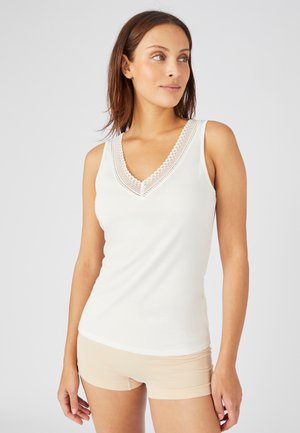 Top bianco senza maniche con scollo a V profondo e bordo in pizzo decorativo. Tessuto morbido e liscio con una silhouette aderente. Short color carne sotto.