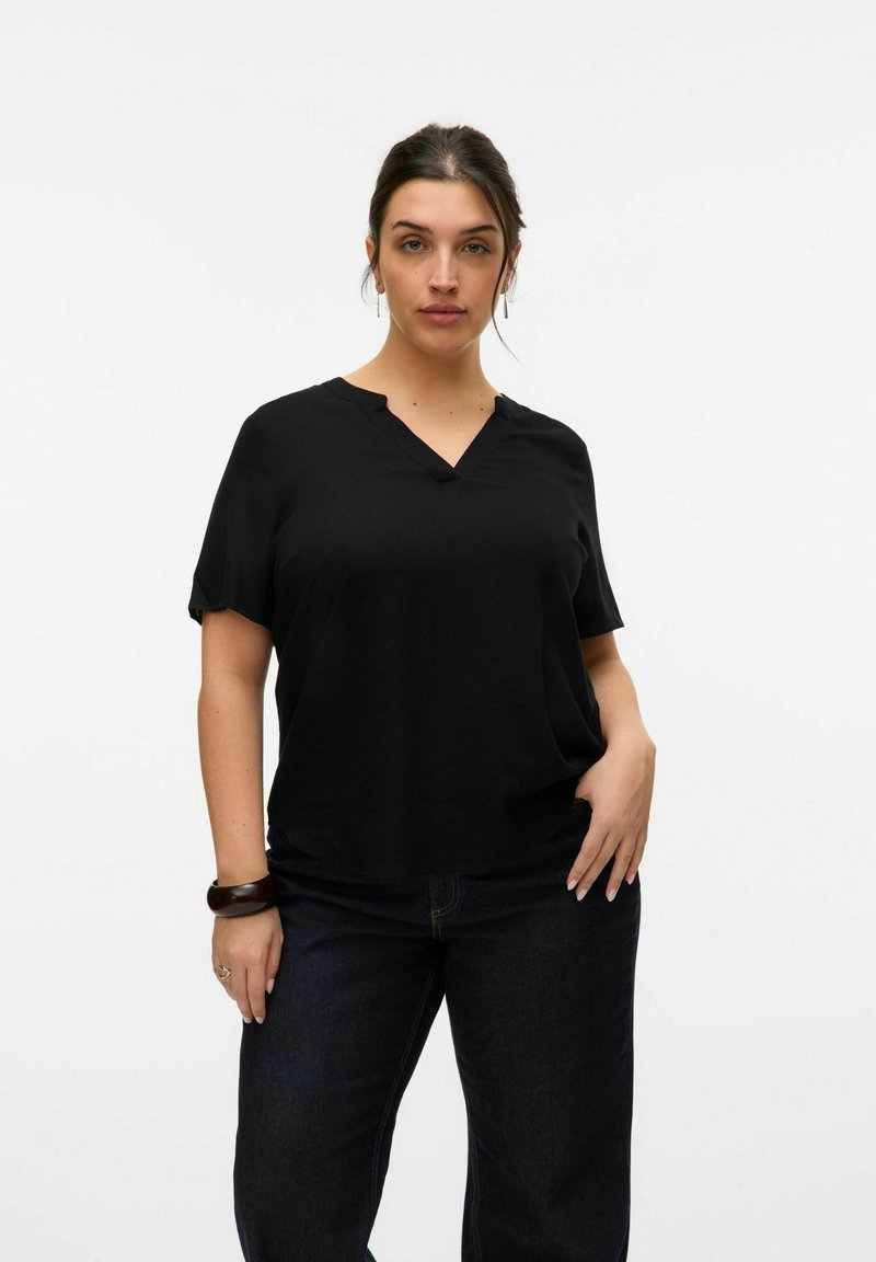 Top negro de manga corta con escote en V y corte relajado, fabricado en una tela suave. Combinado con jeans oscuros, acentos de hardware mínimos.