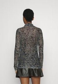 Longsleeve, przezroczysta czarna bluzka z teksturowanym wzorem przypominającym łuski; ma wysoki kołnierz i ciasno przylega w talii, zestawiona ze skórzaną spódnicą.