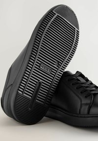 Zwarte sneakers met een gladleren bovenwerk, platte rubberen zool en een gestructureerde buitenzool met uitgesproken ribbels en een logo op de hiel.