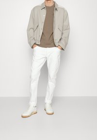 Chaqueta gris claro con cuello, sudadera marrón, pantalones ajustados blancos y zapatillas blancas con suela beige. Atuendo casual. Textura de tela suave.