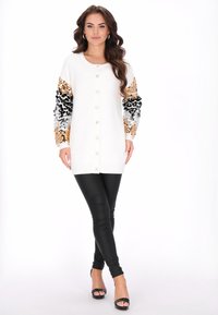 Witte cardigan met mouwen versierd met zwarte, gouden en zilveren pailletten; voorzien van grote knopen, lange mouwen en een iets oversized pasvorm.