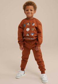 Felpa marrone e pantaloni della tuta abbinati, con illustrazioni di animali e la scritta "INCONTRA I MIEI AMICI A PELLE", abbinati a sneakers bianche.