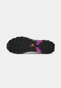 Suela de una zapatilla con una base de goma negra, con patrones hexagonales prominentes y acentos en púrpura y naranja. Diseñada para ofrecer tracción.