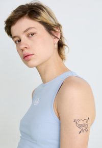 Light blue sleeveless top with a round neckline and a small logo detail, paired with a visible tattoo featuring a heart and banner.