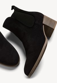 Botines de ante negro con paneles laterales elásticos y tacón de madera apilada. Textura suave, puntera redondeada y detalles de costura en tono.