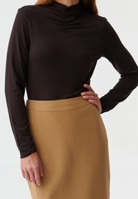 Langærmet, tætsiddende mørkebrun top med samlet halsudskæring, parret med en lysebrun blyantskirt. Tekstureret stof og glatte konturer.