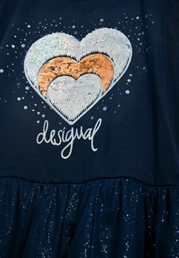 Morska haljina s višeslojnim dizajnom i šljokičastim volanom na rubu. Ukrašena oblikom srca od šljokica i tekstom "desigual" u bijeloj boji.