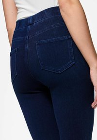 Tamno plave traperice s visokim strukom, elegantnom siluetom, dvije stražnje džepove klasičnog oblika i glatkom teksturom.