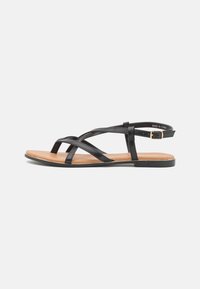 Black synthetic leather sandals with multiple crisscross straps, flat tan sole, and ankle strap featuring an adjustable buckle.