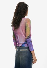 Veelzijdige trui met lange mouwen, in een verloop van paarse, roze en blauwe tinten. Gemaakt met donkerdenim jeans, gezien vanuit de achterkant.