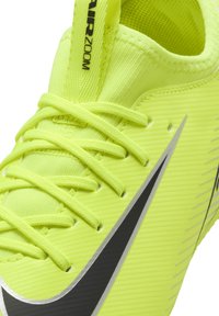Zapatilla deportiva amarilla brillante con material texturizado, swoosh negro de Nike y acentos en gris. Cuenta con cordones y una lengüeta acolchada para mayor comodidad.