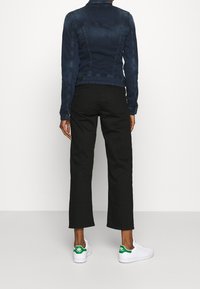 Tmavě modrá džínová bunda s přiléhavým střihem, která má límec a zadní švy. V kombinaci s černými širokými kalhotami a bílými teniskami s zelenými akcenty.