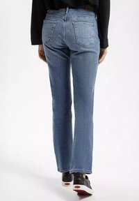 Jasnoniebieskie dżinsy o prostym kroju i średnim stanie, z pięcioma kieszeniami oraz subtelnymi przeszyciami. Noszone z czarnymi trampkami.