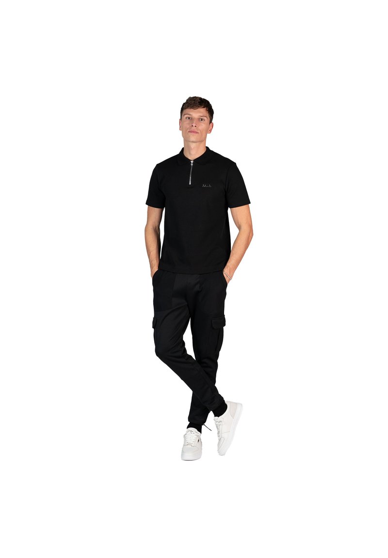 Čierna polokošeľa so zipsom, v kombinácii s čiernymi cargo nohavicami so bočnými vreckami. Model má na sebe biele tenisky. Jednoduchý, elegantný dizajn.