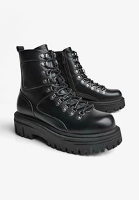 Ghete negre din piele cu șireturi în față, găuri argintii și talpă groasă de cauciuc. Dispune de un fermoar lateral pentru o purtare ușoară.