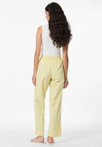 Lichtgele gestreepte broek met een relaxte pasvorm en elastische tailleband. De stof lijkt zacht met een gladde textuur. Er worden platte sandalen gedragen.
