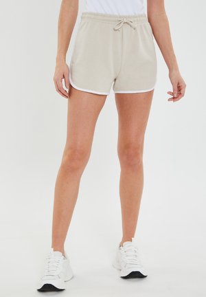 Beige atletiske shorts med hvide sidelogoer, elastisk talje og snor. Lavet af blødt, letvægtsstof.