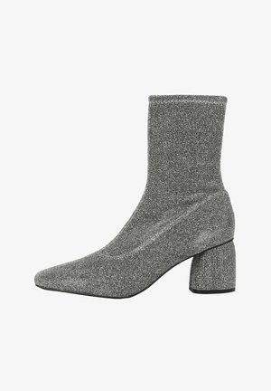 Bottine pailletée argentée avec un design semblable à une chaussette, un bout pointu et un talon épais. Le matériau présente une surface texturée et scintillante.