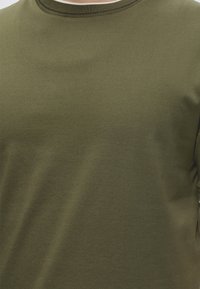 Λαδί πράσινο μπλουζάκι με στρογγυλή λαιμόκοψη και ριμπ λεπτομέρεια στον γιακά, εμφανίζεται στο πάνω μέρος του κορμού, ομαλή υφή υφάσματος.