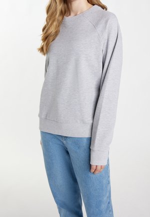 Sudadera de felpa gris con cuello redondo, mangas raglán y puños de canalé, combinada con jeans de color azul claro. Textura suave, ajuste casual.