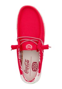 Scarpa di tela rossa con suola in gomma bianca, con dettaglio a farfallino e logo Coca-Cola, interno a fantasia con la scritta "HEY DUDE."