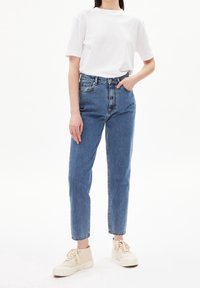 Vaqueros de tiro alto azules con pierna recta, combinados con una camiseta blanca de manga corta. Las zapatillas tienen un tejido texturizado de color crema.