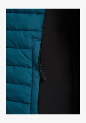 Zbliżenie czarnej kurtki z niebieskim pikowanym panelem i widocznym suwakiem na szwie między dwoma tkaninami.