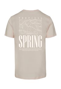 Vaaleanpunainen puuvillapaita, jossa on pehmeä rakenne, ja jossa on valkoinen grafiikka, jossa on sanat "TROPICAL SPRING" sekä yksityiskohtaisia lehtikuvioita.