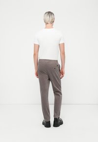 Graue Corduroyhosen mit relaxed Fit, elastischem Bund und Gesäßtaschen-Detail, kombiniert mit einem schlichten weißen T-Shirt und schwarzen Schuhen.