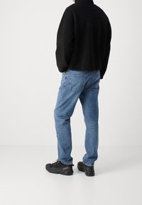 Giacca in pile nera con colletto alto, abbinata a jeans denim azzurri e sneakers nere con materiale strutturato e lacci.