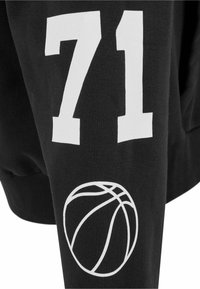 Čierna mikina s bielou potlačou čísla "71" a grafickým zobrazením basketbalovej lopty na rukáve. Vyrobená z mäkkého textilného materiálu.