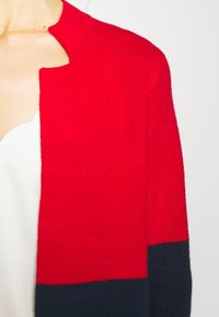Cardigan bicolore rouge et bleu marine avec un col rond, une texture douce et une coupe décontractée, doté d'un tissu en maille et d'un design à l'avant ouvert.