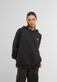 Czarny, oversize'owy hoodie z kieszenią z przodu, z małym złotym logo na lewej piersi. Wygodny, casualowy materiał o miękkiej fakturze.